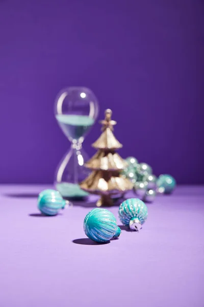 Enfoque selectivo de la Navidad decorativa cerca de bolas azules y reloj de arena sobre fondo púrpura - foto de stock