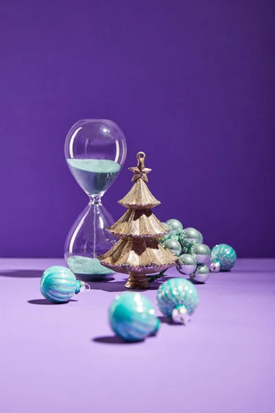 Selektiver Fokus der dekorativen Weihnachten in der Nähe von blauen Christbaumkugeln und Sanduhr auf lila Hintergrund — Stockfoto