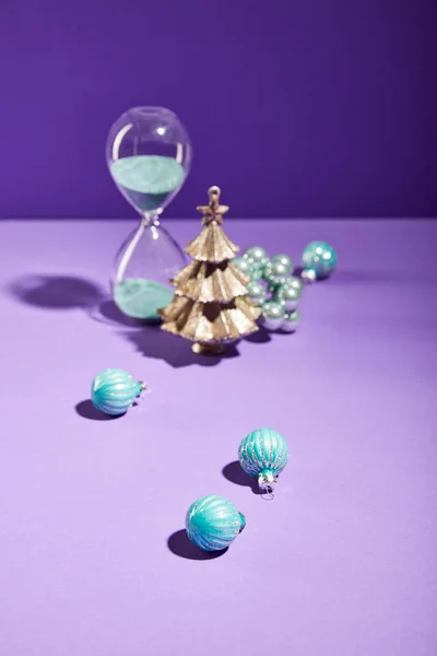 Selektiver Fokus der dekorativen Weihnachten in der Nähe von blauen Christbaumkugeln und Sanduhr auf lila Hintergrund — Stockfoto