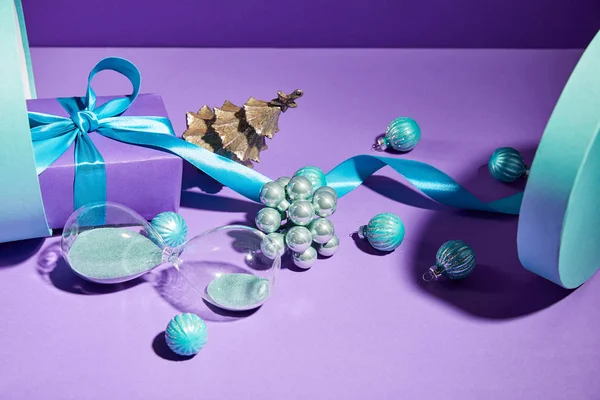 Décoration de Noël et sablier dispersés de boîte cadeau bleue sur fond violet — Photo de stock