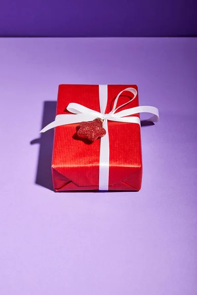 Червона подарункова коробка з вадою на фіолетовому фоні — стокове фото