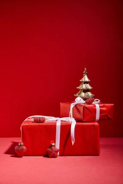 Caixas de presente vermelho e árvore de Natal dourada decorativa com bugigangas no fundo vermelho — Fotografia de Stock