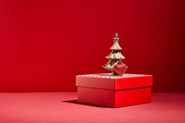 Caja de regalo roja y árbol de Navidad dorado decorativo con adorno sobre fondo rojo - foto de stock