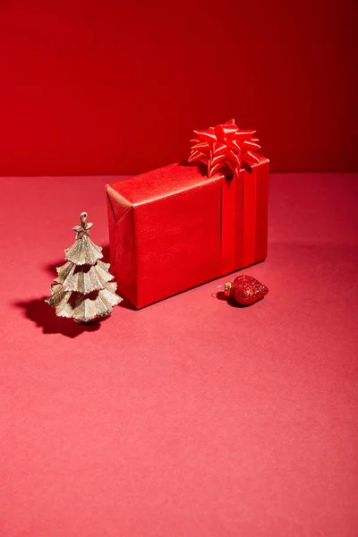 Caja de regalo roja y árbol de Navidad dorado decorativo con adorno sobre fondo rojo - foto de stock