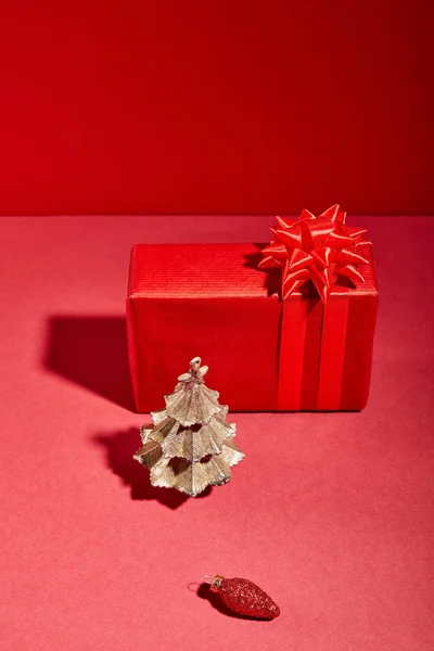 Rote Geschenkschachtel und dekorativer goldener Weihnachtsbaum mit Christbaumkugel auf rotem Hintergrund — Stockfoto