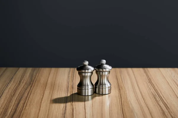 Agitadores de sal y pimienta metálicos en mesa de madera aislada en negro - foto de stock