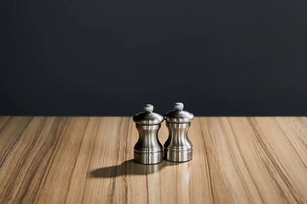 Agitadores de sal y pimienta plateados sobre mesa de madera aislada sobre negro - foto de stock