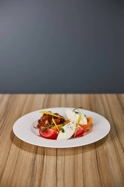 Вкусное блюдо ресторана с баклажанной икрой и помидорами на деревянном столе, изолированном на сером — стоковое фото