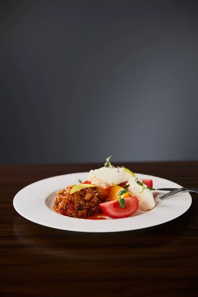 Вкусное блюдо ресторана с баклажанной икрой и помидорами подается на деревянном столе со столовыми приборами на черном фоне — стоковое фото