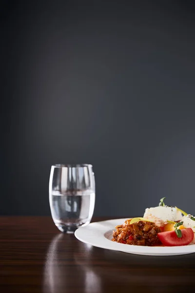 Delizioso piatto del ristorante con caviale di melanzane e pomodori serviti su tavolo di legno con acqua su sfondo nero — Foto stock