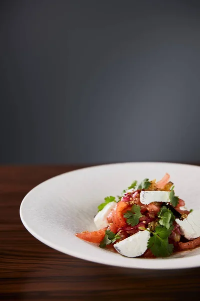Вкусный салат ресторана с сыром подается в белой тарелке на деревянном столе на черном фоне — стоковое фото