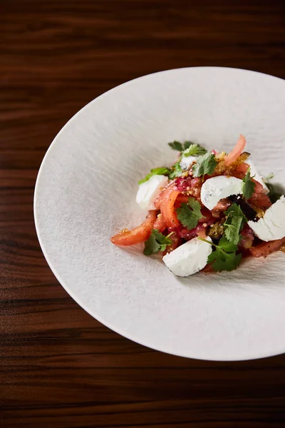 Delicious restaurant salad with cheese served in white plate on wooden table — Stock Photo