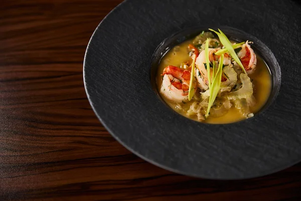 Vue rapprochée d'une délicieuse soupe de restaurant aux crevettes en assiette noire sur une table en bois — Photo de stock