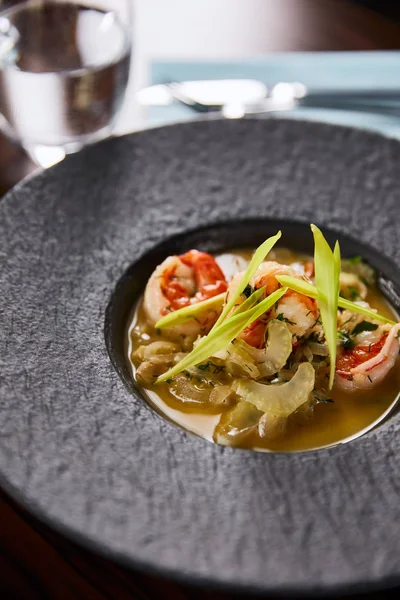 Vue rapprochée d'une délicieuse soupe de restaurant aux crevettes en assiette noire — Photo de stock