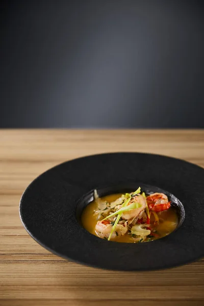Délicieuse soupe de restaurant aux crevettes en assiette noire sur table en bois sur fond noir — Stock Photo