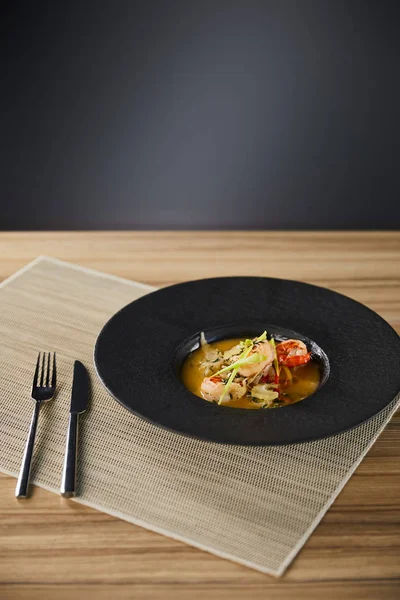 Delicious restaurant soup with shrimps in black plate served on napkin with cutlery — Stock Photo