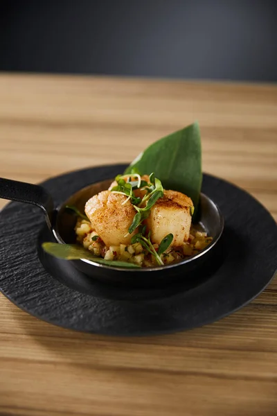 Deliciosos vieiras grelhadas com folhas verdes e microgreens na mesa de madeira no fundo preto — Fotografia de Stock