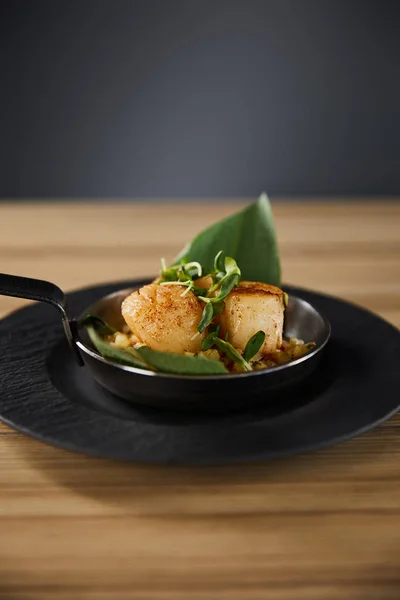 Délicieux pétoncles grillés aux feuilles vertes et microverts sur table en bois sur fond noir — Photo de stock