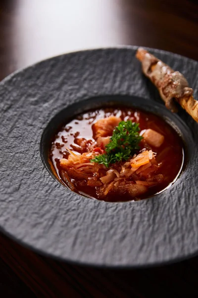 Traditional ukrainian borscht garnished with parsley in black plate — Stock Photo