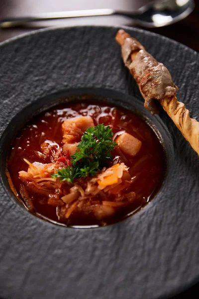 Traditional ukrainian borscht garnished with parsley in black plate — Stock Photo