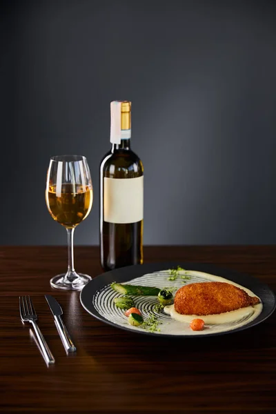 Delicious chicken kiev and mashed potato served on plate near cutlery and white wine on black background — Stock Photo