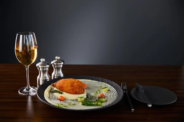 Delicious chicken kiev and mashed potato served on plate near cutlery and white wine on black background — Stock Photo