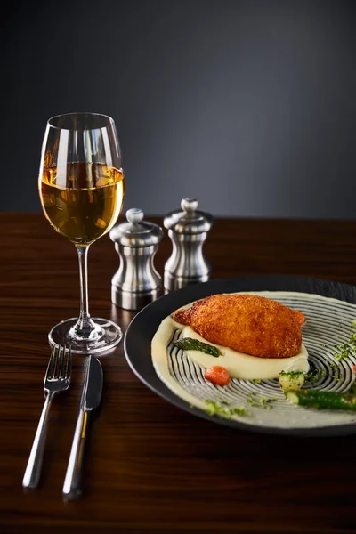 Delicious chicken kiev and mashed potato served on plate near cutlery and white wine on black background — Stock Photo