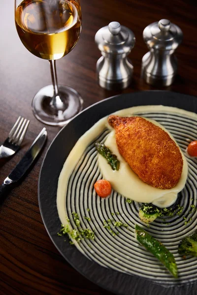 Delicioso pollo kiev y puré de papa servido en el plato cerca de cubiertos y vino blanco - foto de stock