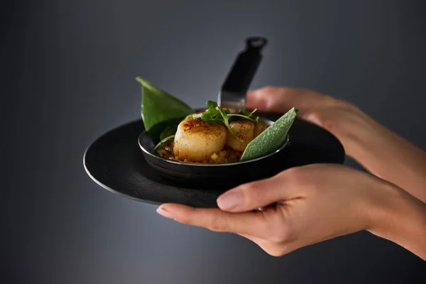 Cropped view of woman holding plate with delicious grilled scallops on black background — Stock Photo