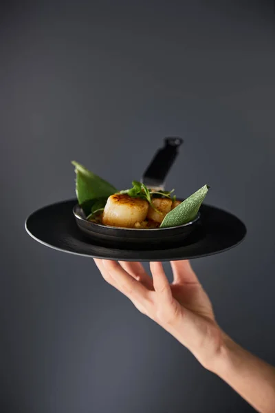 Cropped view of woman holding plate with delicious grilled scallops on black background — Stock Photo