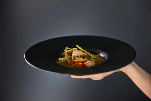 Cropped view of woman holding plate with shrimp soup on black background — Stock Photo