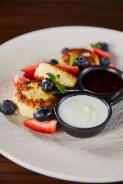 Close up view of traditional Ukrainian dish syrniki with strawberry, blueberry served with jam and sour cream — Stock Photo