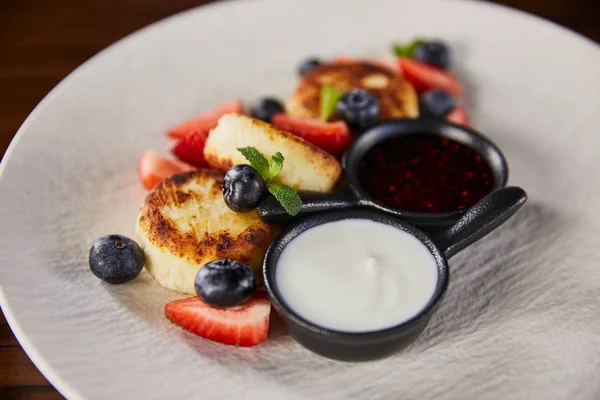 Vista da vicino del tradizionale piatto ucraino syrniki con fragola, mirtillo servito con marmellata e panna acida — Foto stock