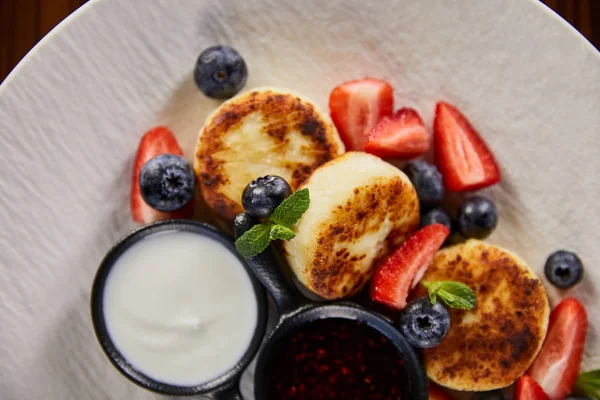 Vista superior de sirniki plato tradicional ucraniano con fresa, arándano servido con mermelada y crema agria - foto de stock