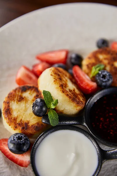 Close up view of traditional Ukrainian dish syrniki with strawberry, blueberry served with jam and sour cream — Stock Photo