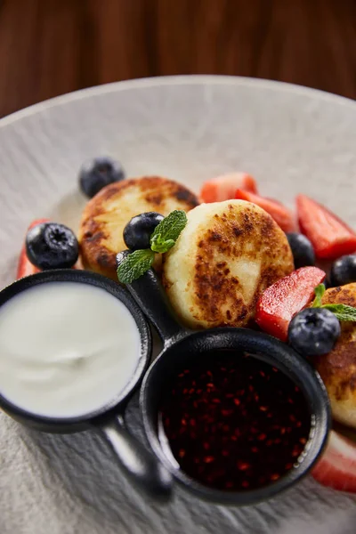 Close up view of traditional Ukrainian dish syrniki with strawberry, blueberry served with jam and sour cream — Stock Photo