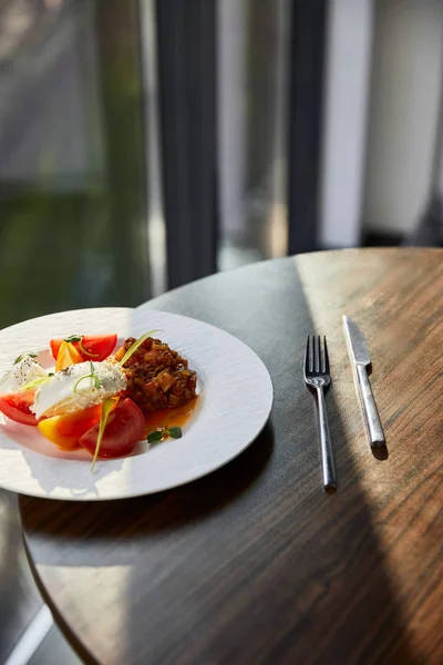 Délicieux caviar d'aubergines avec tomate et beurre servi au restaurant sur table en bois avec couverts au soleil — Photo de stock