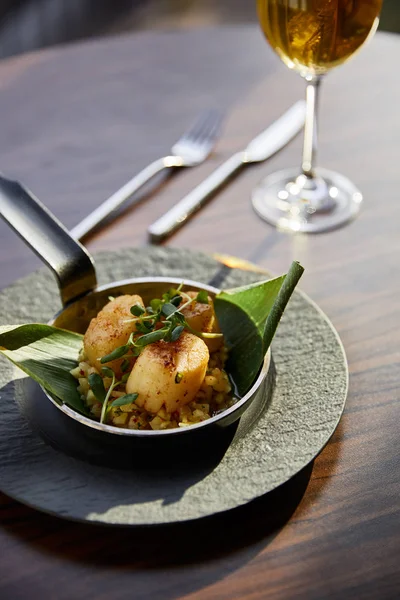 Foco seletivo de deliciosos vieiras grelhadas servidas em panela com microgreens perto de vinho branco à luz do sol — Fotografia de Stock