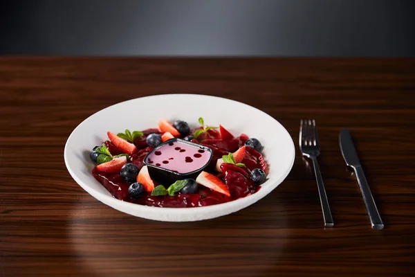 Selektiver Schwerpunkt der traditionellen ukrainischen varenyky mit Beeren in weißem Teller mit Sauce in der Nähe von Besteck auf Holztisch serviert — Stockfoto