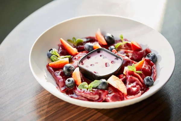 Close up view of traditional Ukrainian varenyky with berries served in white plate with sauce on wooden table in sunlight — Stock Photo