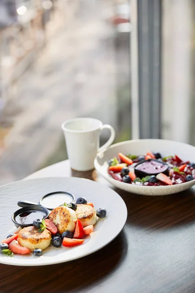 Selective focus of traditional Ukrainian varenyky and syrniki with berries served in white plate with sauce near cup on wooden table in restaurant — Stock Photo