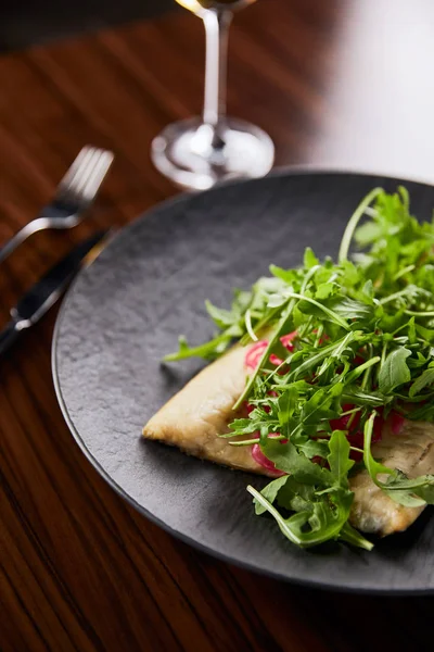 Selective focus of tasty restaurant fish steak with lime and arugula on wooden table near cutlery — Stock Photo