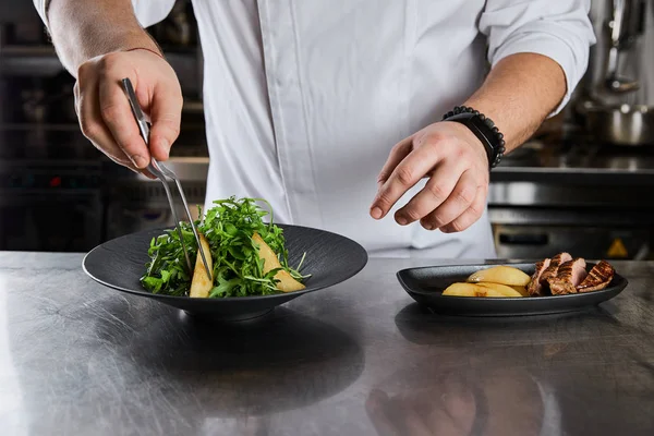 Частичный вид блюда шеф-повара с рукколой, мясом и картофелем на кухне в ресторане — стоковое фото