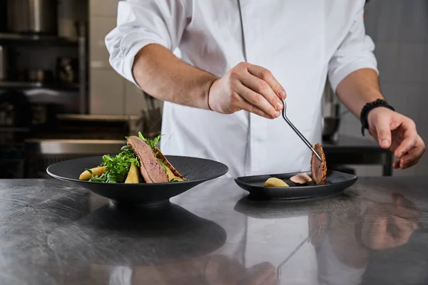 Cropped view of chef cooking dish with arugula, meat and potato at kitchen in restaurant — Stock Photo