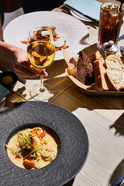 Cropped view of woman holding glass of white wine near soup with shrimps in restaurant — Stock Photo