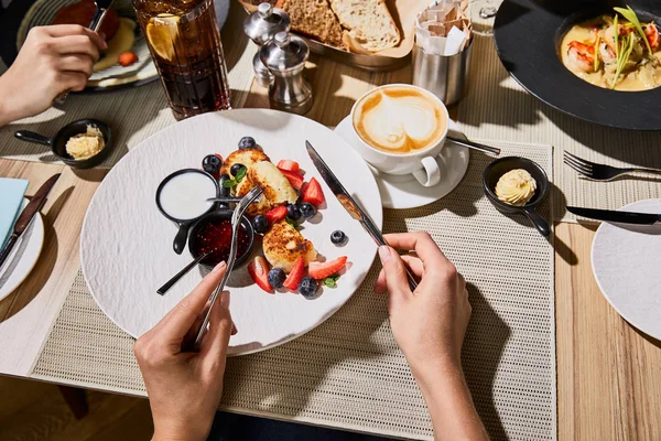 Abgeschnittene Ansicht einer Frau, die köstliche Syrniki während des Abendessens mit Freunden im Restaurant isst — Stockfoto