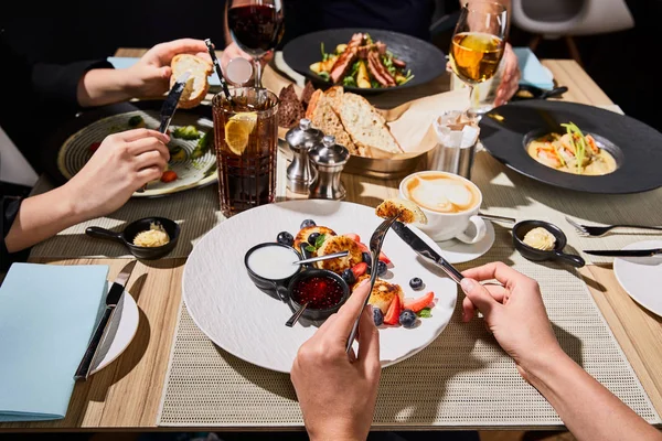 Vista cortada de mulher comendo delicioso syrniki durante o jantar com amigos no restaurante — Fotografia de Stock