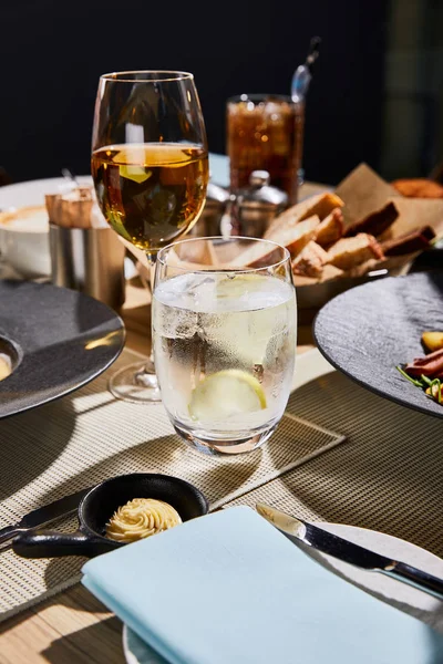 Agua con hielo y limón cerca de la copa de vino blanco en la mesa en el restaurante - foto de stock