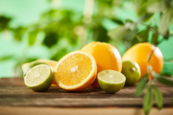 Mise au point sélective de la coupe, des oranges entières et des chaux sur la surface en bois — Photo de stock