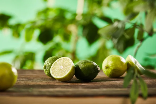 Selective focus of cut and whole limes on wooden surface — Stock Photo